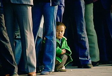 Small child crouching among adults queuing in Tiananmen Square to enter the Forbidden City, Beijing, China (Peking).