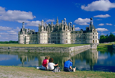 Tourists at the Chateau Chambord in the Loire Valley, France (Val de la Loire).  Impressive turrets and towers are reflected in the waters of the moat which was originally to repel invaders from the castle.