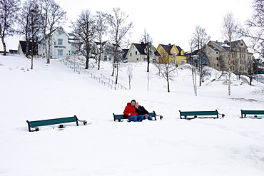 Young couple sitting on park bench in deep snow in Tromso, Norway