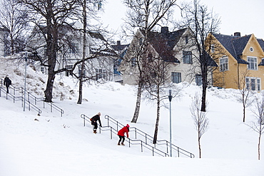 Young woman takes photographs as her friend hangs onto handrail to avoid slipping on the steps in snowy Tromso, Norway