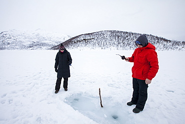 Couple ice- fishing on frozen lake in the Arctic Circle on Ringvassoya Island in the region of Tromso, Northern Norway