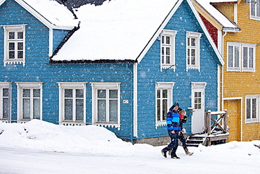 Couple walk past traditional wooden buildings along Storgata in the quaint area of Tromso, in the Arctic Circle in Northern Norway