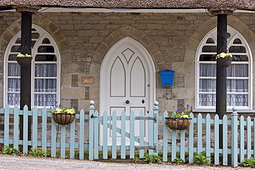 Quaint traditional cottage with thatched roof, gothic style arched door , hanging baskets and paling fence, Cornwall, England, UK