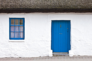 Blue and white traditional whitewashed thatched cottage in Ardmore Village, County Waterford, Ireland