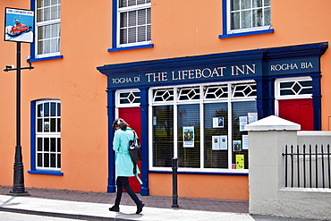 Young woman strolls past The Lifeboat Inn traditional bar in Courtmacsherry, West Cork, Ireland