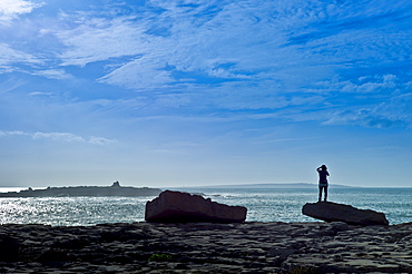 Woman taking photographs of the Arran Isles at Doolin tourist resort in County Clare, West Coast of Ireland