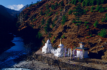 Buddhist shrines and prayer flags at the river's edge in a valley in Bhutan.