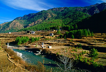 Homes at the foot of mountains in Bhutan. Bridge crossing the river.