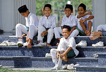 Young boys putting shoes and socks back on after visiting Shah Alam muslim mosque in Kuala Lumpur, Malaysia