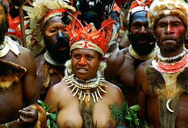 Bare-breasted tribeswoman and tribesmen wearing face paints, bone necklaces and feathered headdress during  a gathering of tribes at Mount Hagen in Papua New Guinea