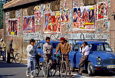 Bollywood ' film posters advertising the latest movies in Agra, India.  Young men chatting together while pushing their bicycles.