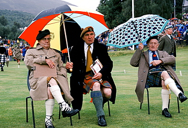 Scottish judges in tartan kilts shelter from rain at the Braemar Royal Highland Gathering, the Braemar Games in Scotland