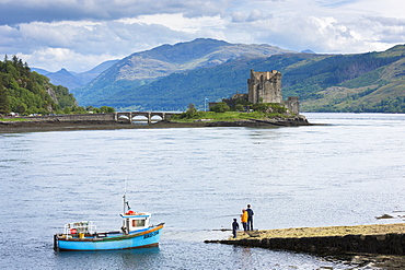 Fishermen fishing by Eilean Donan Castle, a Highland fortress, with Saltire Scottish flag flying in Loch Alsh at Dornie, Kyle of Lochalsh in the western hIghlands of Scotland, United Kingdom, Europe