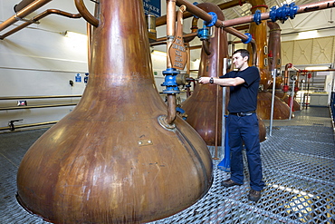 Stillsman inspecting copper spirit stills in the Stillshouse at Talisker Whisky Distillery making single malt whisky in Carbost on Isle of Skye, Scotland, United Kingodm, Europe