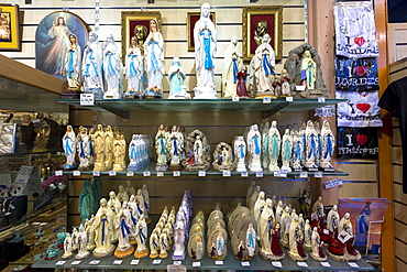 Religious icons and statues of Our Lady and St. Bernadette on shelves in shop at pilgrimage location of Lourdes, Pyrenees, France, Europe