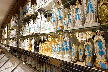 Religious icons and statues of Our Lady and St. Bernadette on shelves in shop at pilgrimage location of Lourdes, Pyrenees, France, Europe