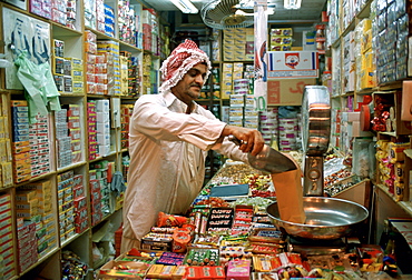 A shopkeeper in a sweet and grocery store in Kuwait City in Kuwait weighing sweets for a customer.