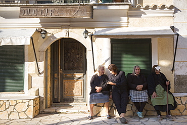 Elderly Corfiot women wearing traditional black clothes sitting relaxing in village square of Krini, Corfu, Greek Islands, Greece, Europe