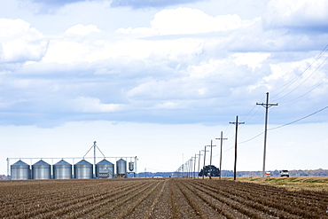 Power lines along Mississippi Delta trail road US Highway 65 and grain silos for crop storage near New Ellton Louisiana, USA