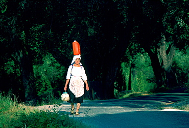 A local woman walking while carrying a can on her head and a pot in her hand, Corfu Island, Greek Islands