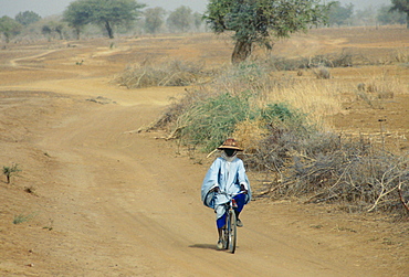 A local man wearing a sunhat rides a bicycle on the road to Sebba through the desert drought areas of Burkina Faso (formerly Upper Volta)