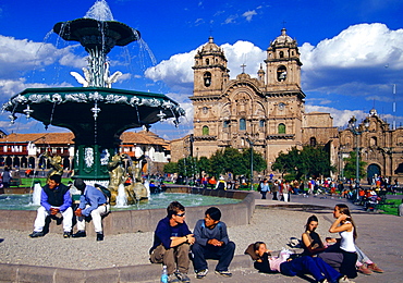 Young people gather in Plaza de Armas  square by the fountain in Cuzco in front of La Compania church in the ancient capital of the Inca Empire, Peru, South America