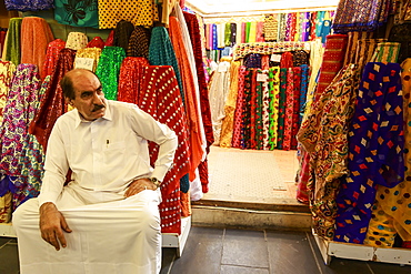 Shopkeeper seated outside his shop surrounded by  colourful material, Souq Waqif, Doha, Qatar, Middle East