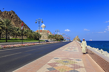 Man wearing dishdasha walks along Mutrah Corniche with national flags, flower beds and Giant Incense Burner, Muscat, Oman, Middle East