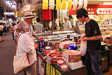 Shoppers make purchase at Omicho fresh food market, busy and colourful covered streets lined by stalls, Kanazawa, Japan, Asia