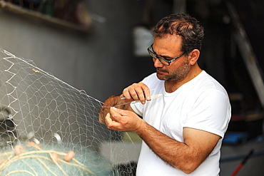 Marina Corricella, fisherman carefully mends fishing nets, Procida Island, Bay of Naples, Italy, Europe