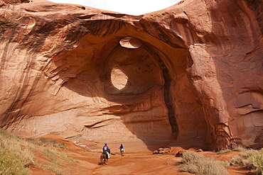 Horse riding trip, tourist with Navajo guide pass under rock arch, Monument Valley Navajo Tribal Park, Utah Arizona, United States of America, North America