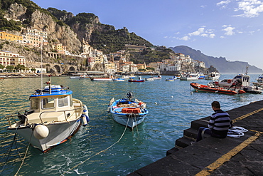 Fisherman working on harbour quayside with view towards Amalfi town and fishing boats, Costiera Amalfitana (Amalfi Coast), UNESCO World Heritage Site, Campania, Italy, Europe