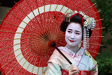 Portrait of smiling geisha in floral robes with red umbrella in summer, Kyoto, Japan, Asia