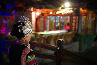 Young woman wearing traditional Yunnan clothing shot from behind in a nightly scene in Lijiang Old Town, Lijiang, Yunnan, China, Asia 