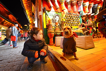 Young girl sitting next to a dog that is wearing bandana and sweater, Lijiang, Yunnan, China, Asia 
