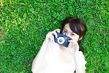 Young Woman Lying on Grass Holding Camera