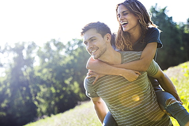 A couple, a man giving a young woman a piggyback, walking through a flower meadow in summer.