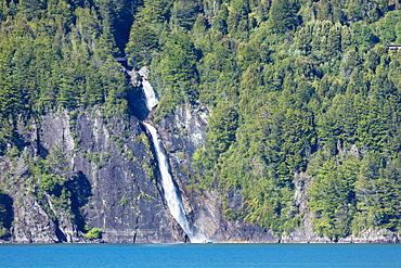 A boat in front of a waterfall on Puelo Lake in the Tagua Tagua reserve, Patagonia, Chile, South America