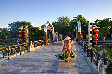 A woman carrying baskets on a yoke over the Lantern Bridge in Hoi An, Quang Nam, Vietnam, Indochina, Southeast Asia, Asia