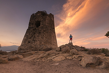 Hiker admires sunset from the stone tower overlooking the bay, Porto Giunco, Villasimius, Cagliari, Sardinia, Italy, Mediterranean, Europe