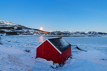 The blue light of dusk on the typical house of fishermen framed by the frozen sea, Fjordbotn, Senja, Troms County, Norway, Scandinavia, Europe