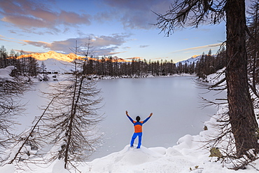 Hiker admires Lago Azzurro completely frozen at dawn, Spluga Valley, Province of Sondrio, Valtellina, Lombardy, Italy, Europe