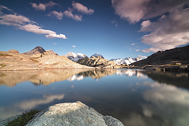 Pink clouds and peaks reflected in water at sunset, Fuorcla, Surlej, St. Moritz, Canton of Graubunden, Engadine, Switzerland, Europe