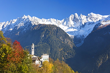 The colorful trees frame the alpine church and the snowy peaks, Soglio, Bregaglia Valley, Canton of Graubunden, Swiss Alps, Switzerland Europe