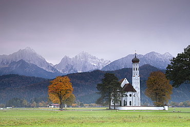 Pink sunrise on St. Coloman Church surrounded by woods and mist of autumn, Schwangau, Bavaria, Germany, Europe