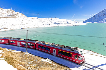 Bernina Express train in the snowy valley surrounded by Lake Bianco, Bernina Pass, Canton of Graubunden, Engadine, Switzerland, Europe