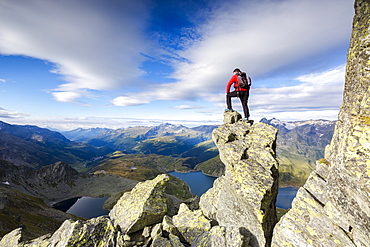 Hiker on top of rocks admires the blue Lake Montespluga in summer, Chiavenna Valley, Valtellina, Lombardy, Italy, Europe