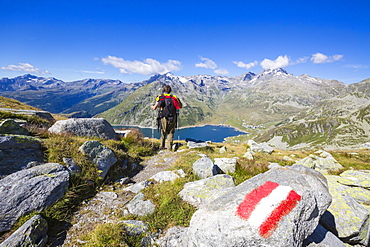 Hiker admires the blue Lake Montespluga and the rocky peaks in summer, Chiavenna Valley, Valtellina, Lombardy, Italy, Europe