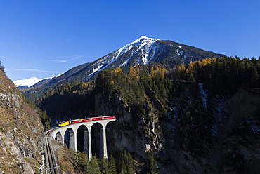 Bernina Express passes over Landwasser Viadukt surrounded by colorful woods, Canton of Graubunden, Switzerland, Europe