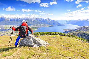 Hiker on green meadows admires Lake Como framed by snowy peaks, Montemezzo, Alpe Zocca, Lombardy, Italian Lakes, Italy, Europe